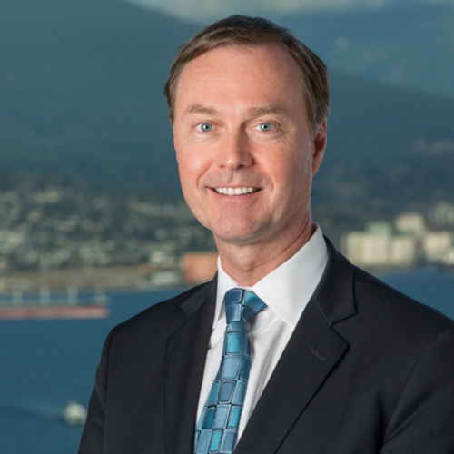 Man in a suit and tie smiling with water and mountains in the background.